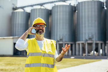 engineer using cellphone in front of blurred grain silos © cherryandbees