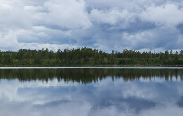 Rainclouds over a Swedish lake inside a forest with the water creating a mirror reflection in the water of the clouds and trees. 