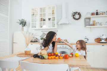 Smiling mom and daughter cooking fruits and vegetables in the Scandinavian-style kitchen. Healthy food. Happy family