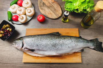 Close-up keta fish, whole on the cutting board of the kitchen table next to olives tomatoes and mushrooms. Healthy sea food. Homemade cooking