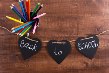 Colored  pencils and back to school text on heart shaped blackboard pieces. Wooden desk, garland,...