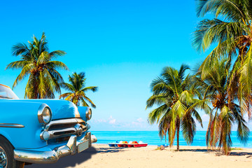 Der tropische Strand von Varadero in Kuba mit amerikanischem Oldtimer, Segelbooten und Palmen an einem Sommertag mit türkisfarbenem Wasser. Urlaub-Hintergrund.