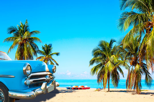 The tropical beach of Varadero in Cuba with american classic car, sailboats and palm trees on a summer day with turquoise water. Vacation background.