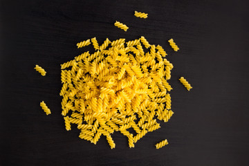 A pile of pasta spiral fusilli on black background