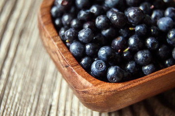 Bilberries in a bowl on brown wooden background, many fresh dark blue berries on table (European blueberries)
