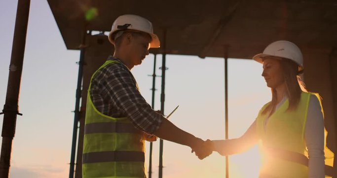 Building, teamwork, partnership, gesture and people concept - close up of builders hands in gloves greeting each other with handshake on construction site.