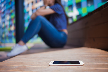 A smartphone lying in the foreground, blurred background, girl, crying, covering face while sitting...