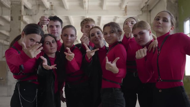 Professional dancer girls and boys enjoying hip hop moves performing freestyle dance together in an abandoned building. Crowd in same stage costumes emotionally showing part of performance with hands.