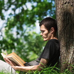 Young Caucasian man or student reading a book in the Park. Summer time and outdoor recreation