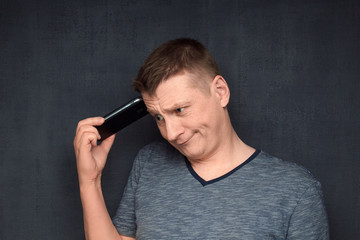 Portrait of funny and puzzled man scratching head using phone