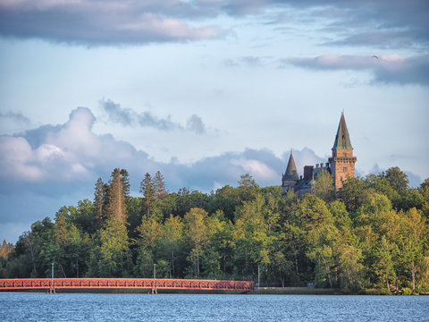 Picture of beatiful ancient castle in the forest with red bridge in front of it. Sunset light coming from cloudy sky