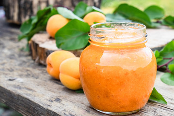 Apricot jam in a glass jar and ripe apricots on a wooden table.