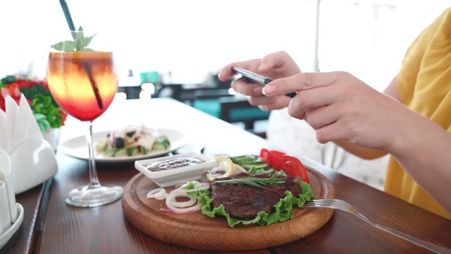 Food blogger hands using smartphone taking photo of beautiful beef steak on wood table inside the cafe to share on social media. Top view food photo. Lifistyle concept.