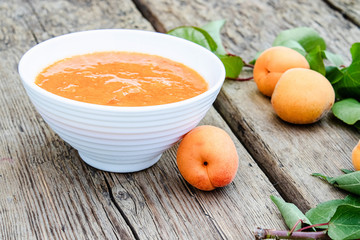 Homemade organic jam in a white bowl and ripe apricots on a wooden table.
