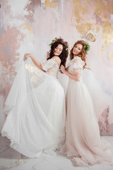 Fototapeta na wymiar Two charming brides in beautiful spring wreaths on their heads. Beautiful young women in wedding dresses