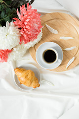 Breakfast of coffee, croissant on a white bed.