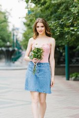 Romantic image of a young girl walking along the summer street of the city in the Park with a bouquet of roses, city recreation and walk