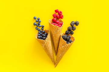 Fresh berries in waffle cones on yellow background top view