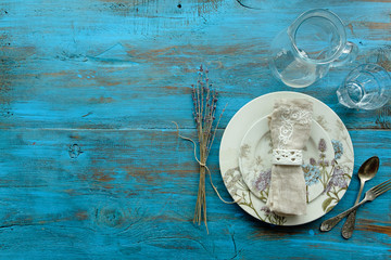 Spring place setting with vintage cutlery, plate with flowers, beige napkin on blue wooden background. Place under the inscription
