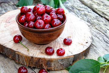 Red cherry in a bowl and green leaves on old wooden boards. Juicy delicious fruit.