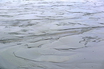 Dirt is the result of wet sand. Abstract gray natural background. Day view of the surface with sky reflections close-up.