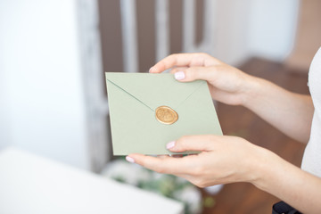 Close-up photo of female hands holding invitation envelope with a wax seal, a gift certificate, a...