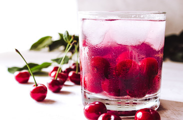 Red cocktail with cherry and ice on a white wooden background. Fresh summer cocktail with cherries and ice cubes.