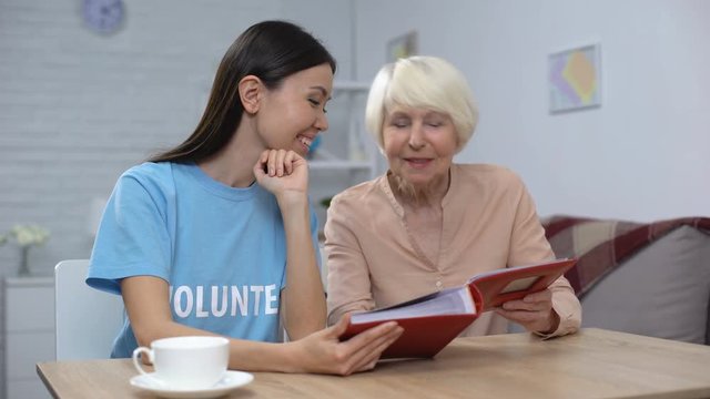 Mature woman showing female volunteer photo album, nursing home leisure, care