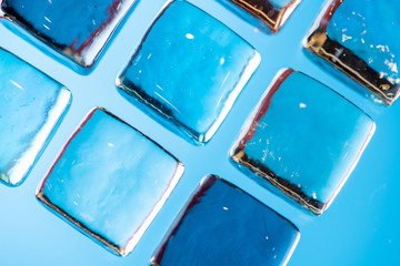 Stylish blue background with transparent ice-like cubes for drinks. Flat lay macro photo.