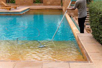 Worker cleaning swimming pool with vacuum tube in the morning.