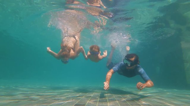 Slowmotion underwater shot of a happy family diving in a swimming pool. Healthy lifestyle, active parents