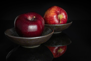 Group of two whole fresh apple red delicious one in front in a dark ceramic bowl isolated on black glass