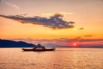 Fototapeta na wymiar Ferry boat to the sea at sunset in the background of mountains and sun beams, run from Keramoti city to Thassos island in Greece
