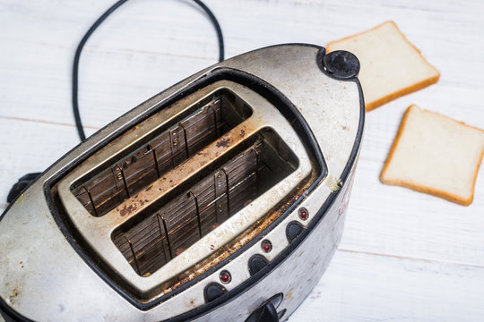 Dirty old toaster with bread on a white wooden background.