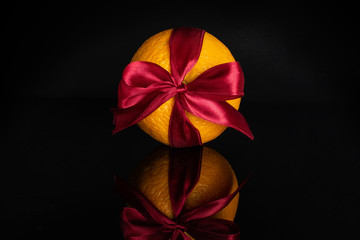One whole fresh sweet orange with a red bow isolated on black glass