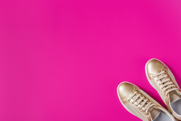 Pair of golden female sneakers on pink background