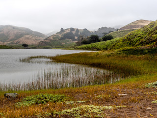 Obraz premium Rodeo Lagoon on a foggy morning featuring the lake shore, grass and the hills in the background