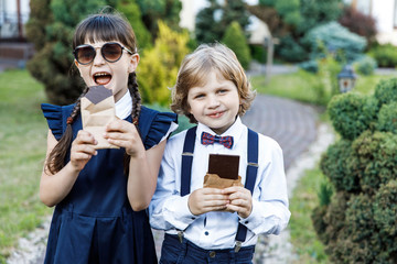 Cute blond guy and cute girl, school year fun time outdoors. Children eat chocolate. Children dressed in school uniform play games in the park