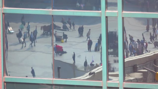 CLOSE UP: Distorted view of pedestrians in the reflection of a large office building window in the business district of Beijing. People walking across city square are reflected in the mirrored windows