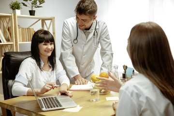 Fototapeta premium Smiling nutritionists showing a healthy diet plan to patient. Young woman visiting a doctor for having a nutrition recommendations. Concept of healthy lifestyle and food, medicine and treatment.