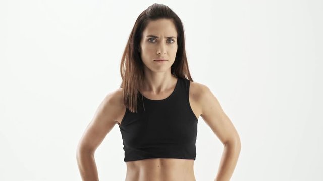 Upset beautiful sporty brunette woman in black sportswear shaking her head and gesturing with hand because of disagreeing with someone over white background isolated
