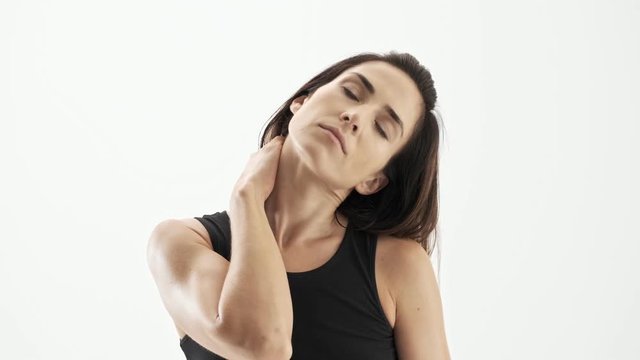 Displeased beautiful sporty brunette woman in black sportswear feeling exhausted and massaging her neck over white background isolated