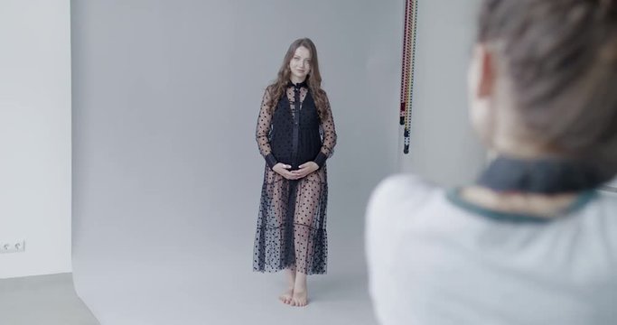Backstage of the photo shoot: Photographer starts taking photos of a beautiful caucasian pregnant model. Studio photoshoot with professional camera. 4K RAW graded footage 24fps