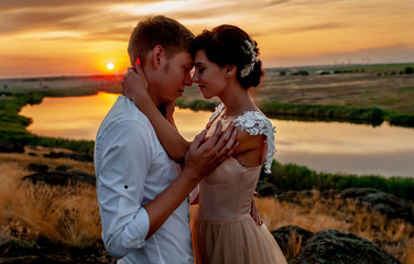 a loving couple, a guy and a girl kiss and hug at sunset on a mountain against the background of the river