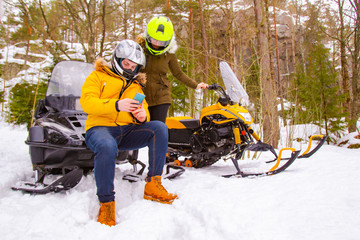 A young married couple travels in the winter forest on snowmobiles. A man looks at his phone geolocation. Loving couple having fun in winter on snowmobiles. Outdoor activities.