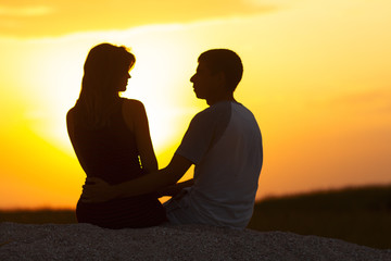 silhouette of a loving couple at sunset sitting on sand on the beach, the figure of a man and a woman in love, a romantic scene in nature, a family vacation, summer rest