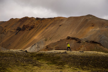Beautiful woman is moving purposefully in front of mountain. Cloudy background. Landmannalaugar, Iceland