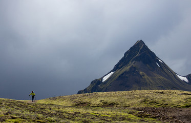 Beautiful woman is moving towards in front of big mountain. Sunlight and cloudy background. Landmannalaugar, Iceland