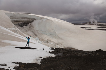 Beautiful woman is standing in front of many broken crevasses and fins of an icefall. Beautiful landscape with steam columns and dramatic sky background. Landmannalaugar, Iceland