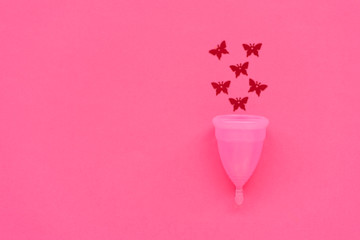 Pink menstrual cup with red glitters in butterfly shape on pink background. Female intimate hygiene concept. Top view